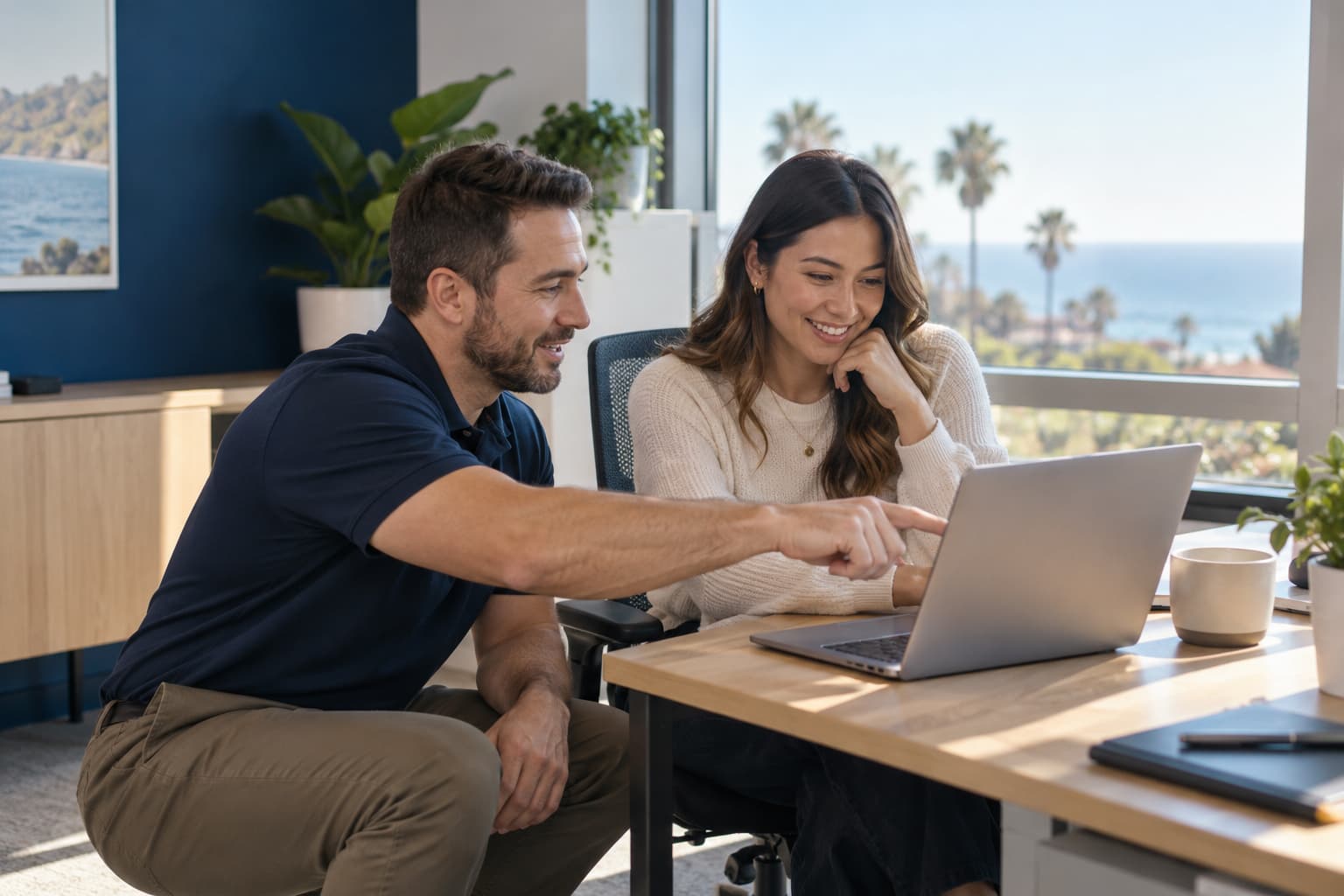 A technician helping an employee at her laptop in a bright office with an ocean view